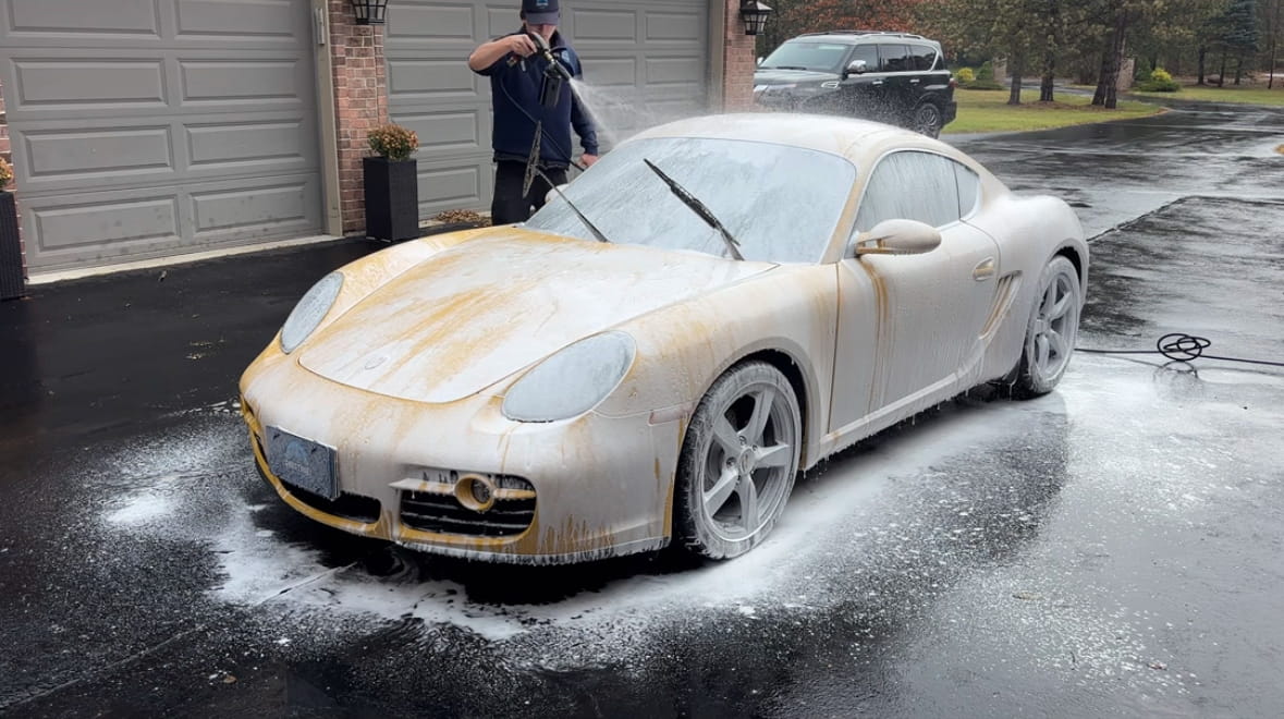 Technician foam washing a yellow Porsche Cayman in a customer's driveway