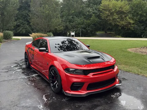 Red widebody Dodge Charger with a black hood on a wet driveway after a mobile wash